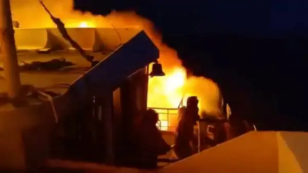 People stand aboard MV June Aster as flames and smoke rise after a fire broke out on the ferry of Palawan coast